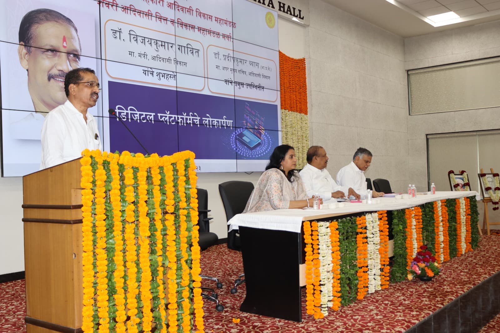 डिजिटल प्लॅटफॉर्म लोकार्पण सोहळ्याचे विहंगम दृश्य — डावीकडे फुलांच्या माळांनी सजवलेल्या व्यासपीठावरून बोलणारे अधिकारी आणि उजवीकडे व्यासपीठावर बसलेले तीन मान्यवर; मागील पडद्यावर ७ ऑगस्ट २०२३ या तारखेसह कार्यक्रमाचा तपशील