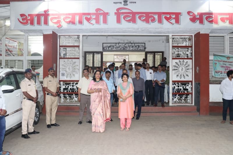 आदिवासी विकास भवनाचे प्रवेशद्वार — पोर्चमध्ये व आसपास सुमारे वीस जण, डावीकडे पोलीस कर्मचारी आणि दर्शनी भिंतीवर वारली शैलीतील चित्रफलक