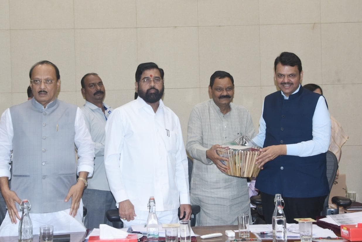 शासकीय बैठकीच्या दालनात मुख्यमंत्री देवेंद्र फडणवीस यांना शबरी नॅचरल्स उत्पादनांची बांबूची मोठी भेटपेटी सुपूर्द करतानाचे दृश्य; टेबलामागे उभे इतर वरिष्ठ मान्यवर