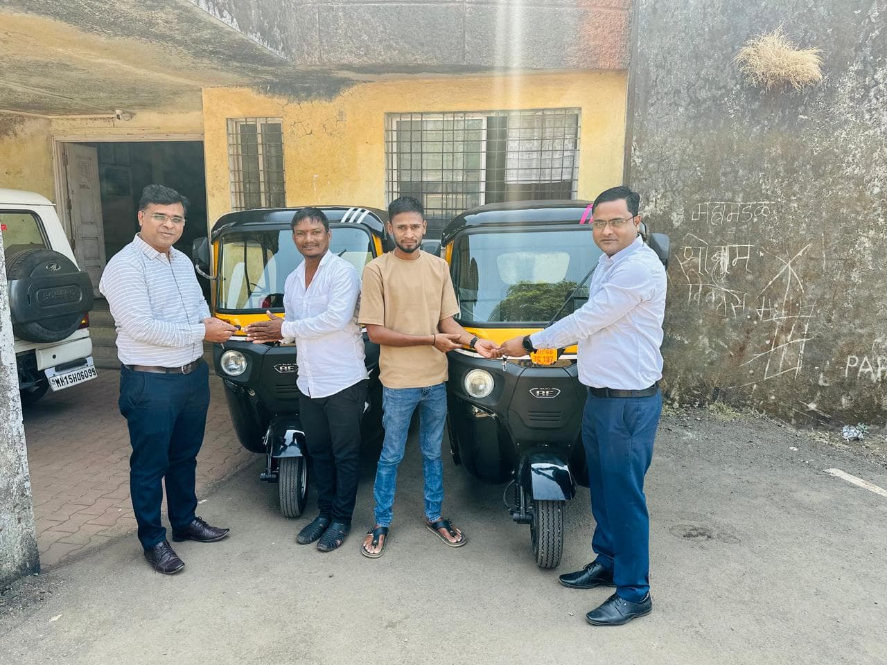 शासकीय इमारतीसमोर दोन नव्या पिवळ्या-काळ्या बजाज रिक्षांमध्ये उभे चार जण, चावी सुपूर्द करताना